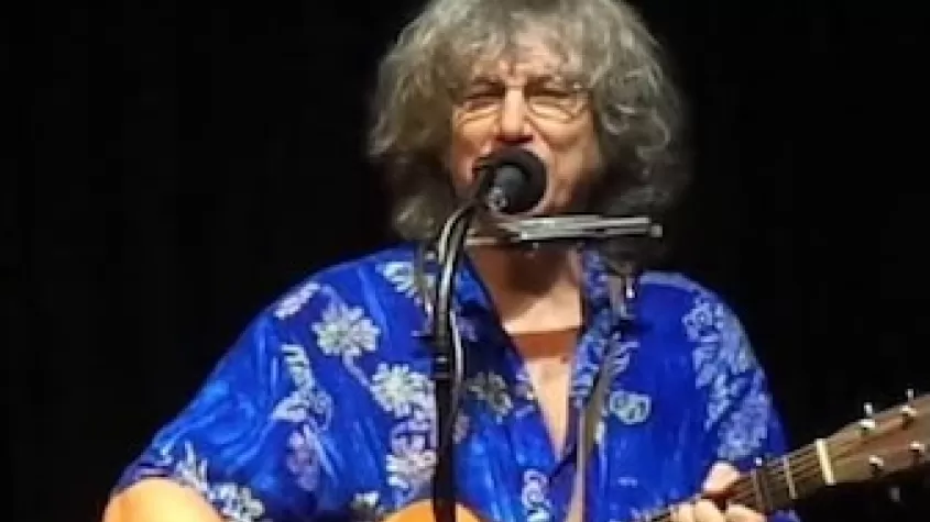 Image of Rod MacDonald playing guitar with a microphone